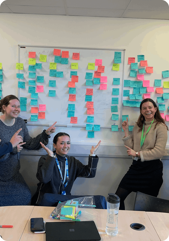 3 woman pointing at whiteboard with postit notes on